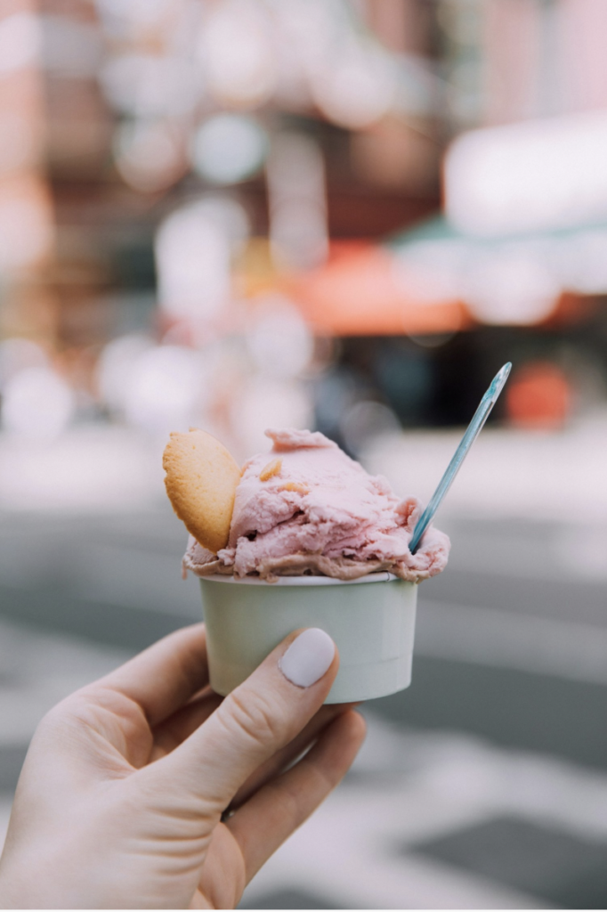 A scoop of pink gelato is held with a little cookie and a plastic spoon